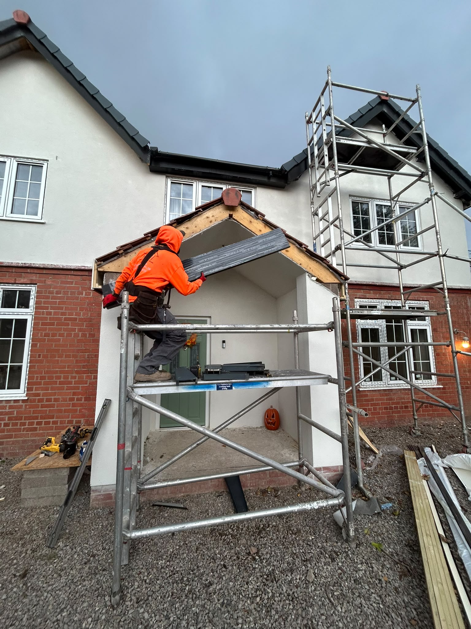 Worker installing tiles on a new porch roof from scaffolding